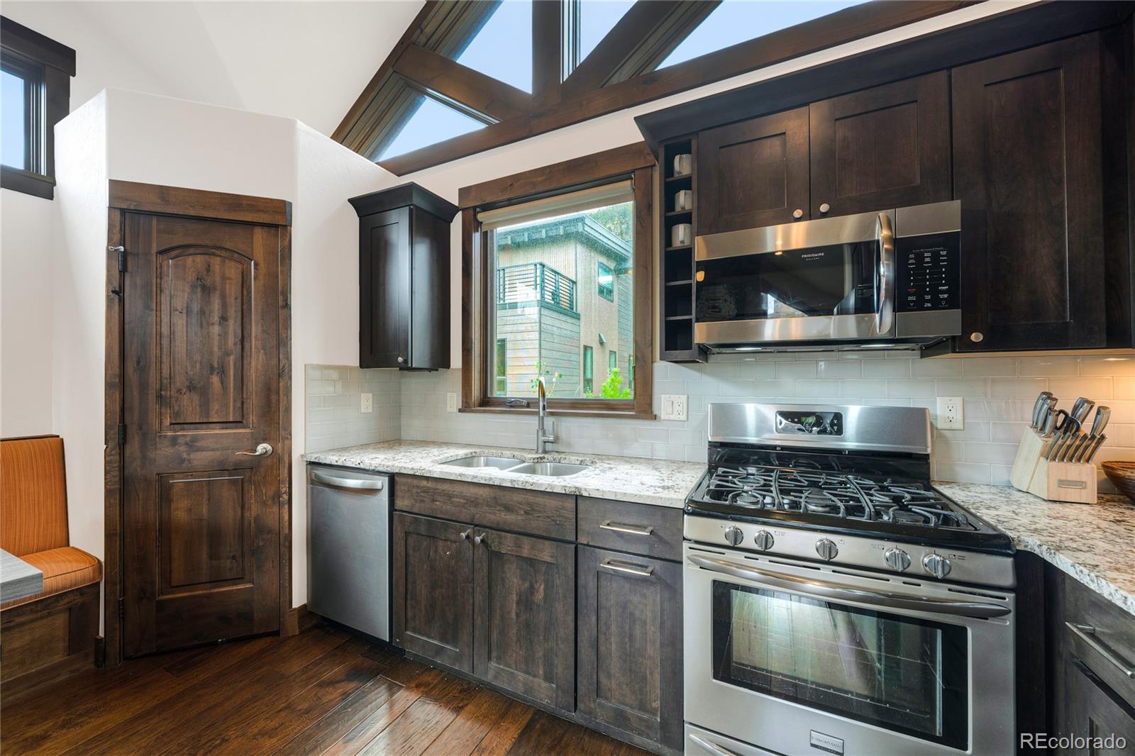 Kitchen with dark wood cabinetry, stainless steel appliances, granite counters, and high clerestory windows.