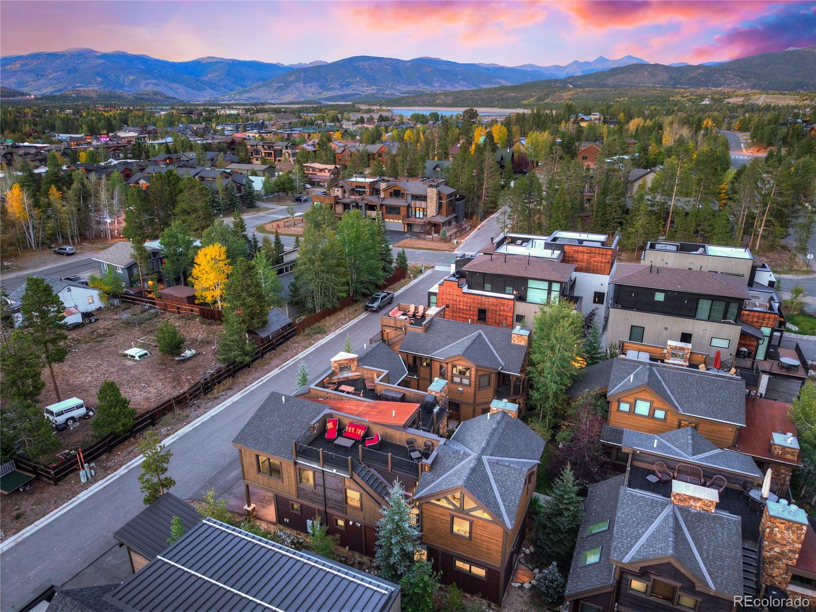 Aerial view of Frisco homes among autumn trees, with a lake and mountain ranges at dusk.