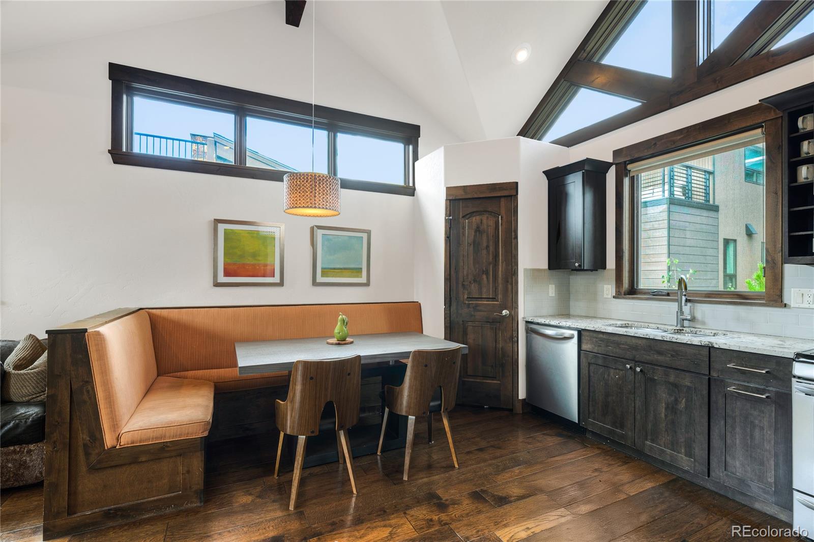 Kitchen dining area with a built-in orange breakfast nook beneath a vaulted ceiling with skylights.