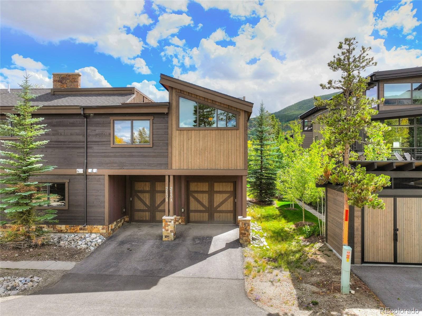 Wood-sided Frisco residence with paired garage doors, evergreens, and a forested mountain backdrop.