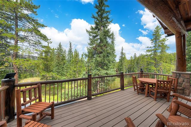 Wooden deck with Adirondack chairs and dining set overlooking evergreen forest.