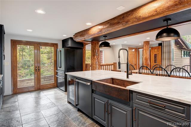Kitchen with a large white island, dark cabinetry, exposed timber beams, and glass doors to the woods.