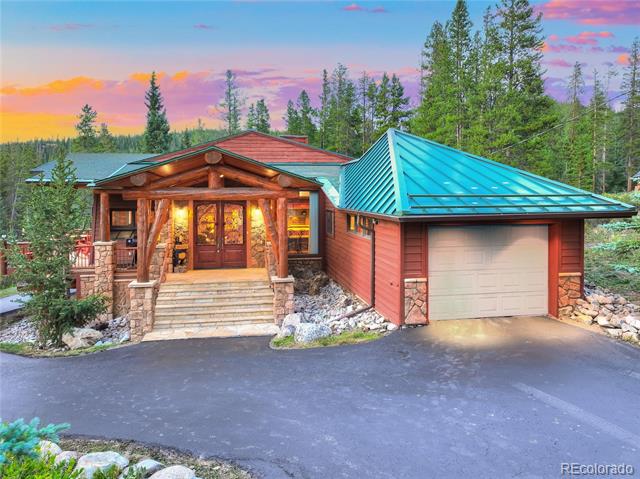 Log home with a turquoise roof, attached garage, and stone-trimmed porch at dusk.