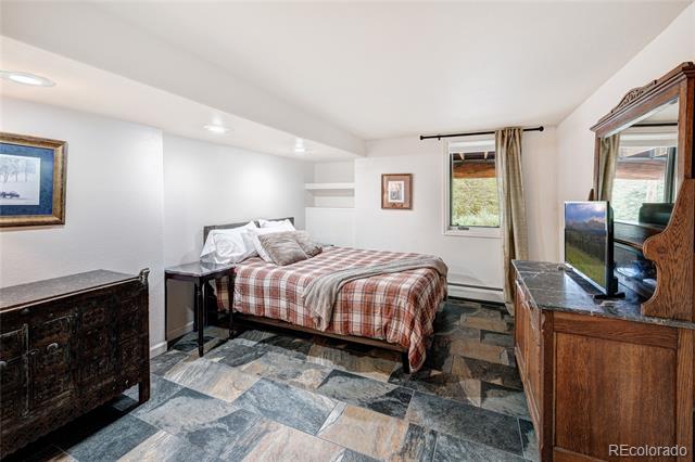 Bedroom with a plaid-covered bed, multicolored stone tile floor, and wooden dresser with mirror.