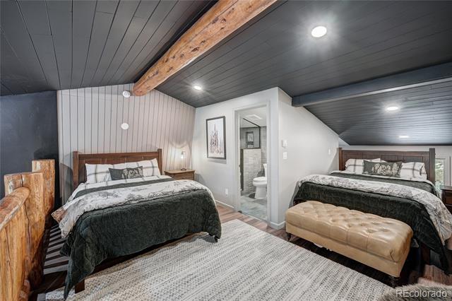 Bedroom with two beds, an exposed wood ceiling beam, and an open bathroom doorway.