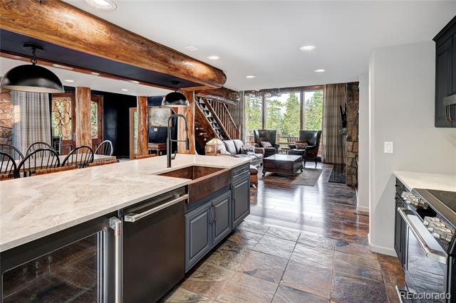 Open kitchen with a stone island and timber beams overlooking a furnished living area.