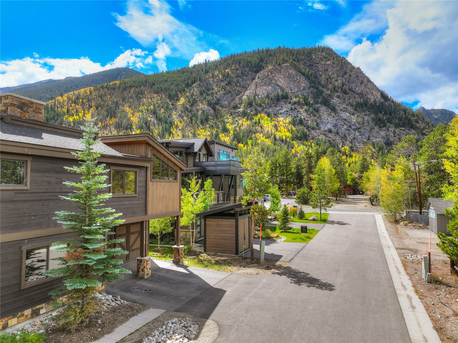 Modern Frisco home beside a quiet street, backed by a rocky, forested mountain with golden autumn trees.
