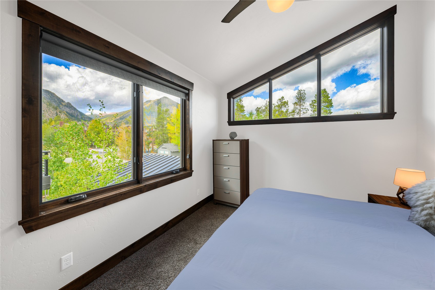 Bedroom with large dark-trimmed windows overlooking trees and mountain slopes.