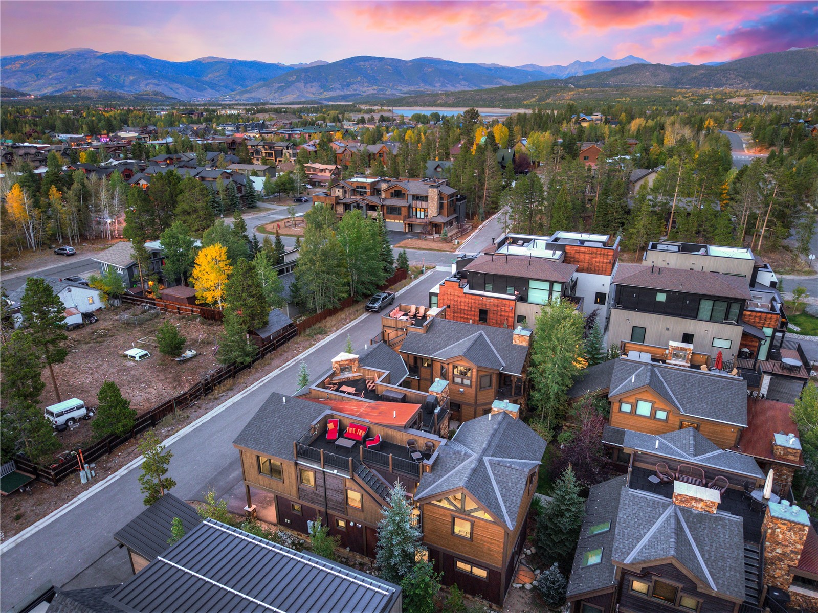 Aerial view of Frisco homes with a lake and mountain range beneath a pink sunset sky.