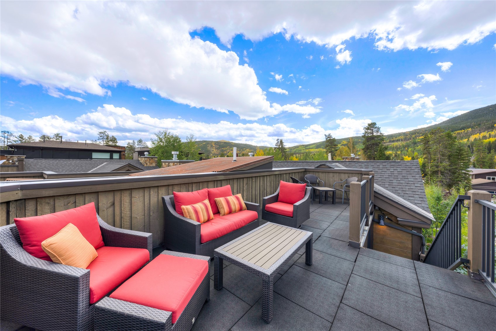Rooftop deck with red-cushioned seating and mountain views amid autumn foliage.