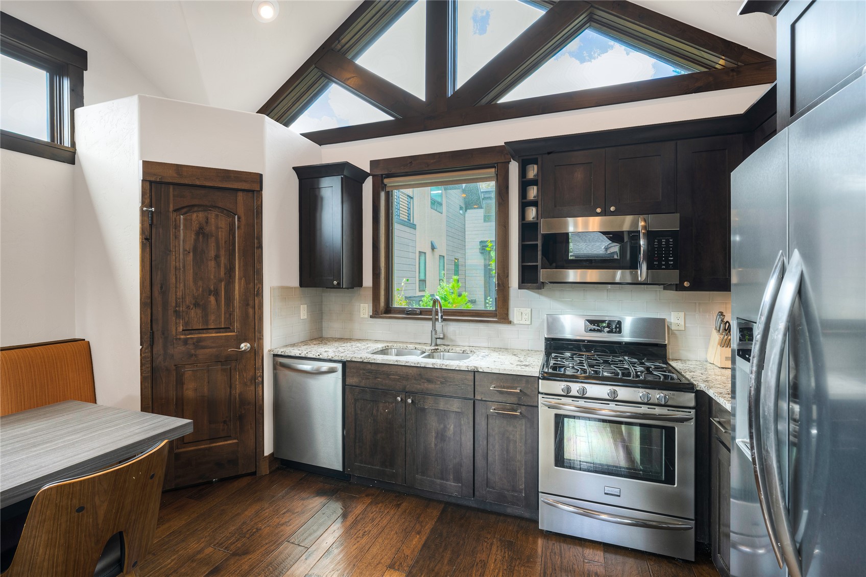 Kitchen with dark wood cabinetry, stainless appliances, granite counters, and dramatic triangular clerestory windows.