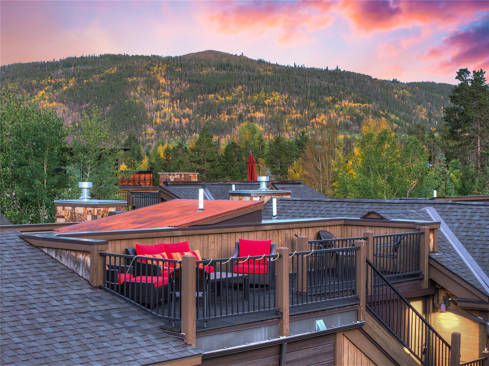 Rooftop deck with red seating overlooking an autumn-colored mountain at sunset.