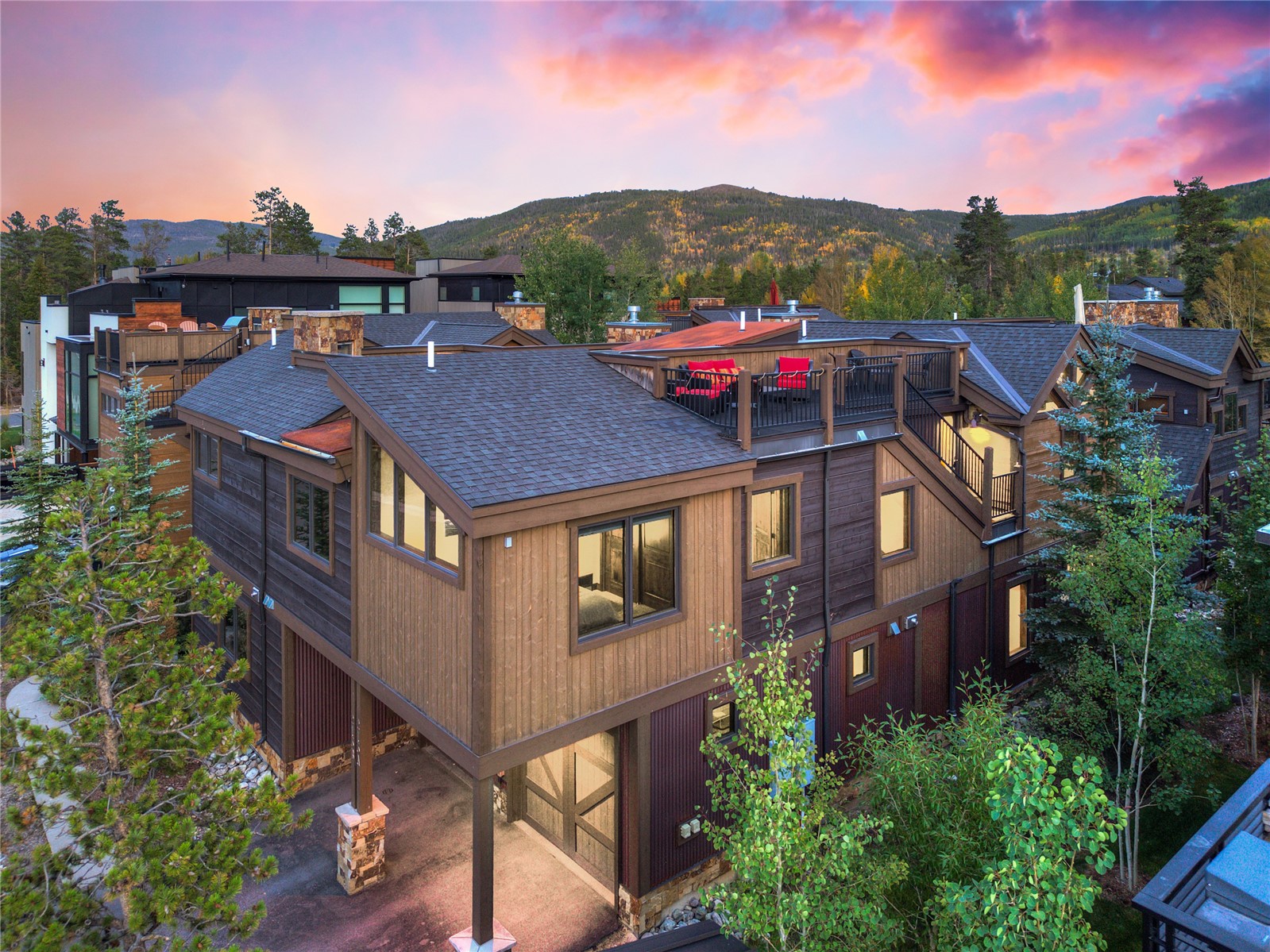 Modern mountain home with balconies and red patio chairs, backed by autumn hills at dusk.