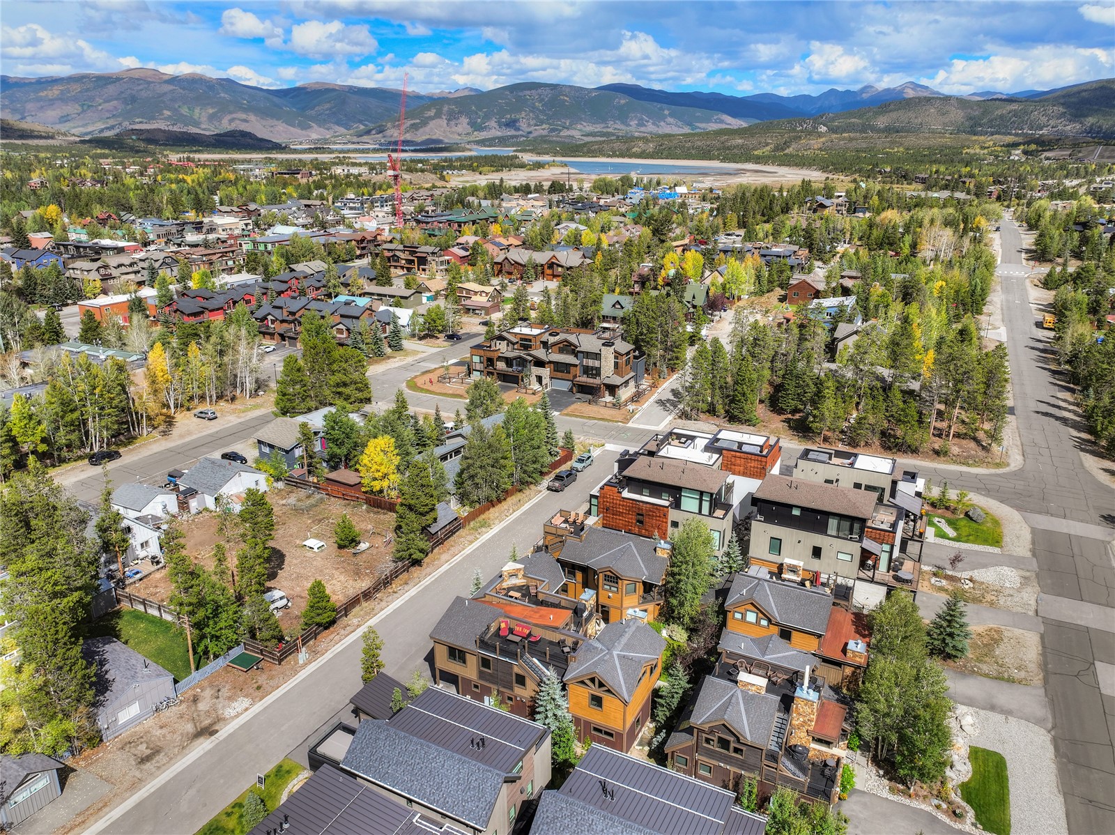 Aerial view of Frisco homes with rooftop decks, a lake, and mountain ranges in the distance.