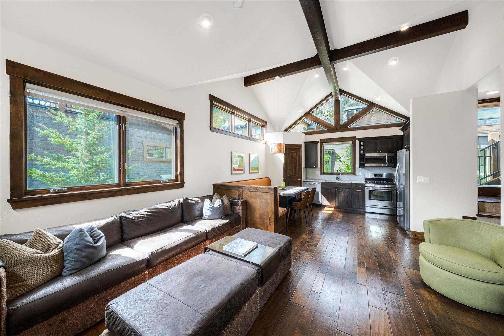 Open-plan living room and kitchen with vaulted timber-beamed ceiling, dark wood floors, and large windows.