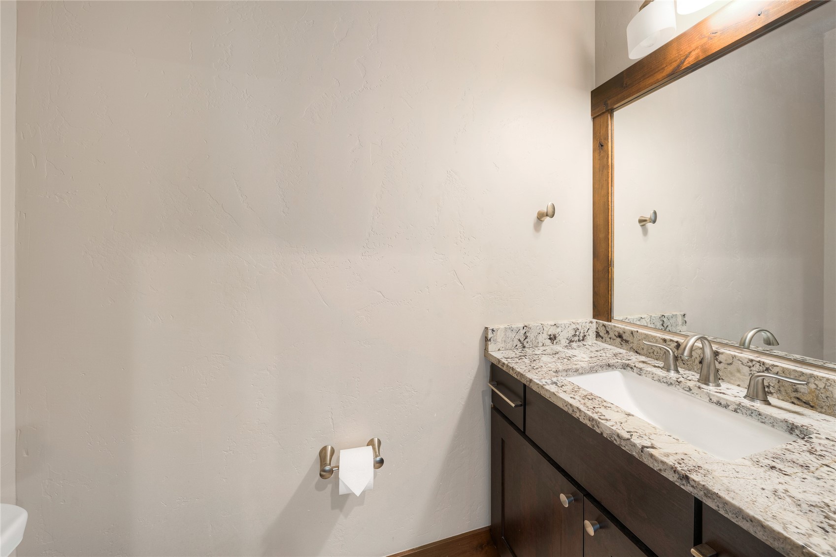 Bathroom vanity with speckled granite countertop, white sink, dark wood cabinets, and a large framed mirror.