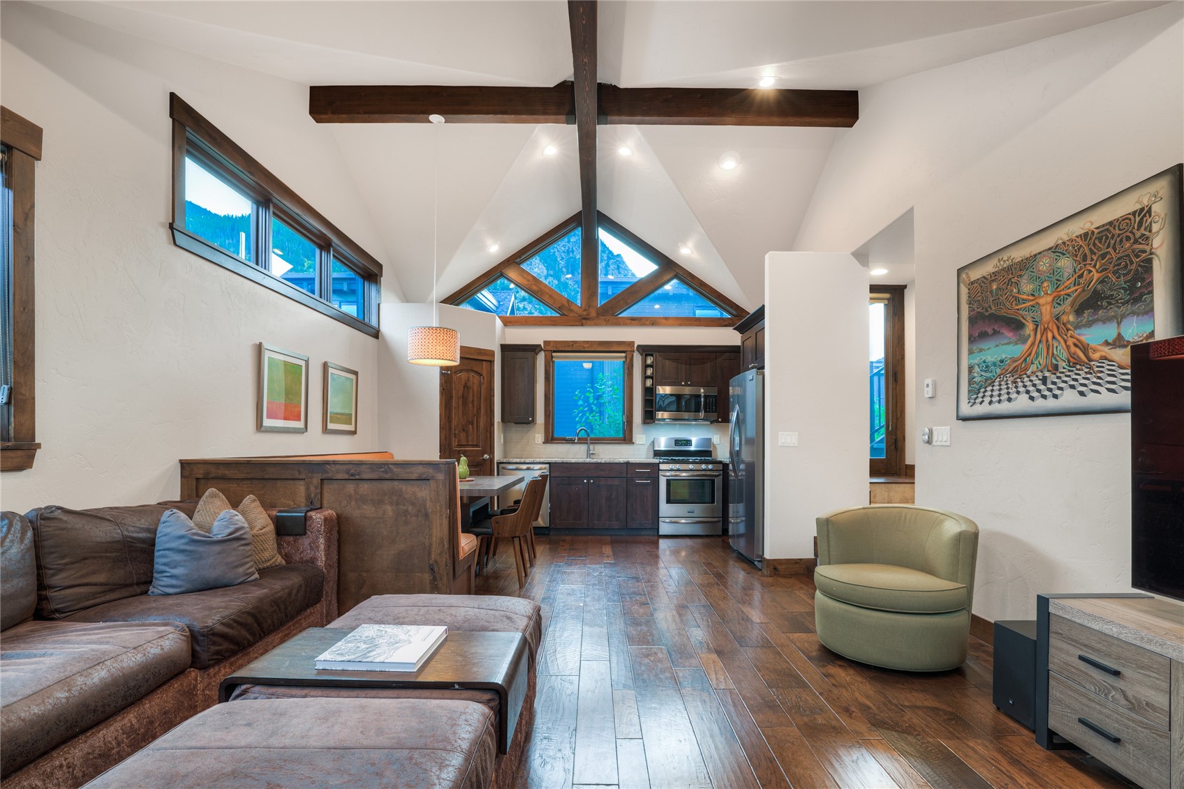 Living room opening to a kitchen beneath vaulted ceilings and exposed beams, with mountain views through large windows.