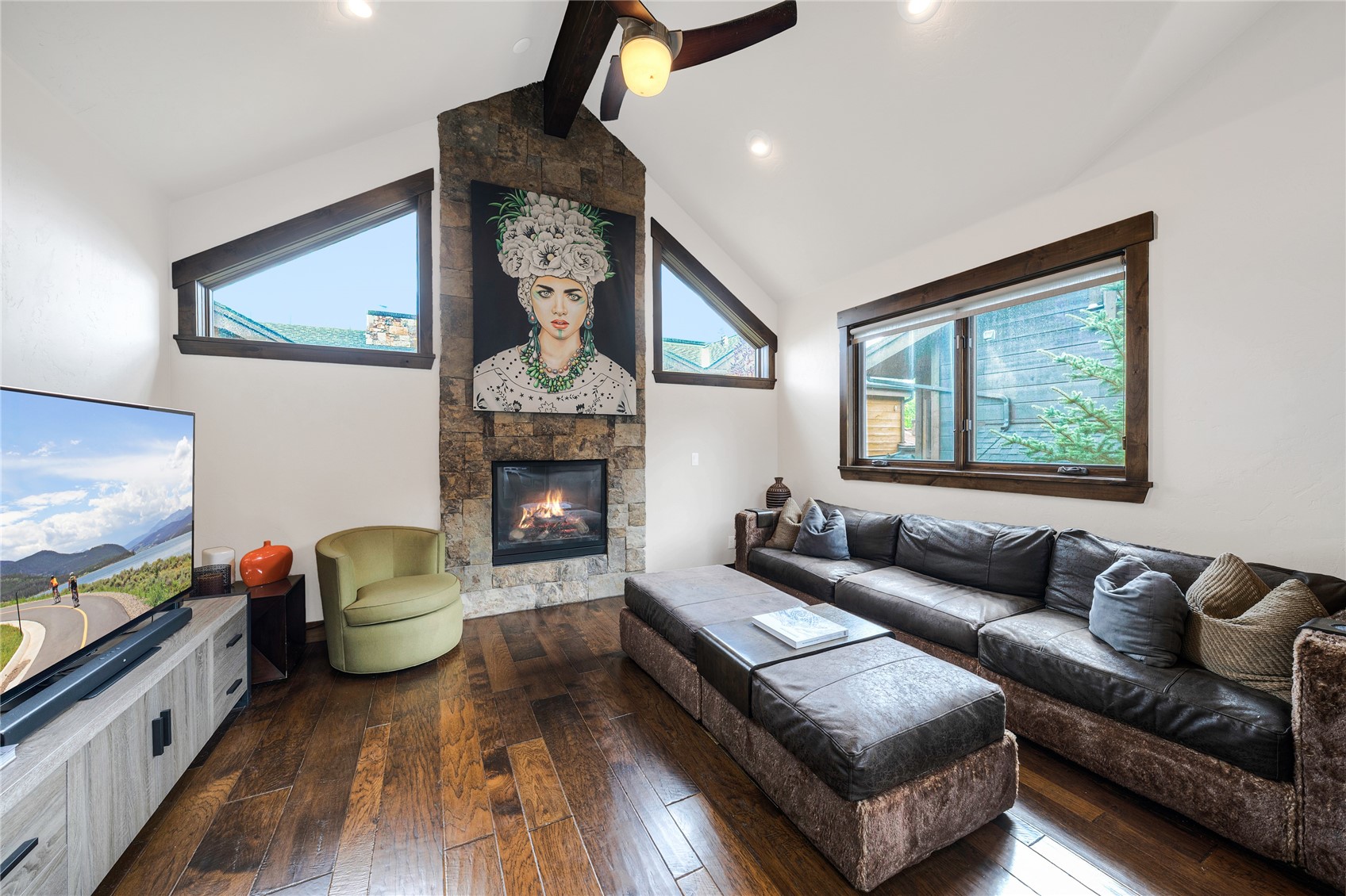 Living room with a stone fireplace, vaulted ceiling, leather sectional, and dark wood floors.