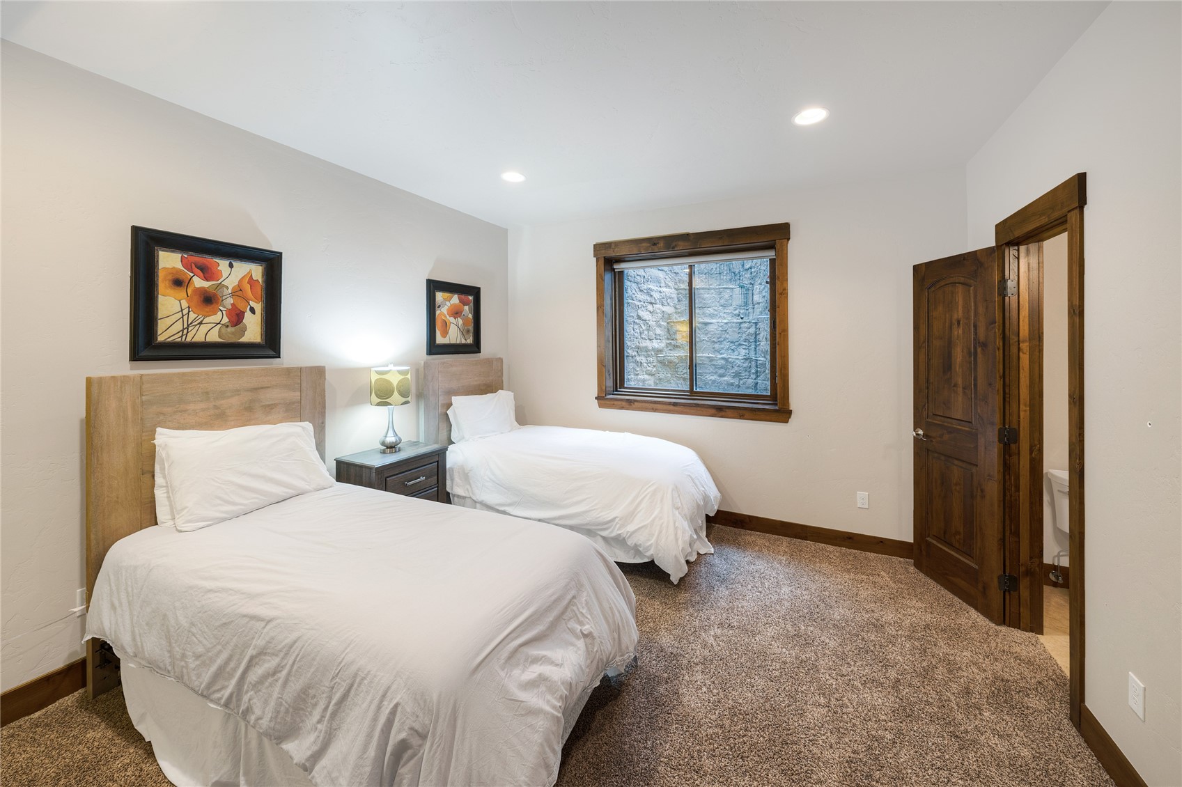 Bedroom with two twin beds, white bedding, dark wood trim, and a window facing a stone wall.