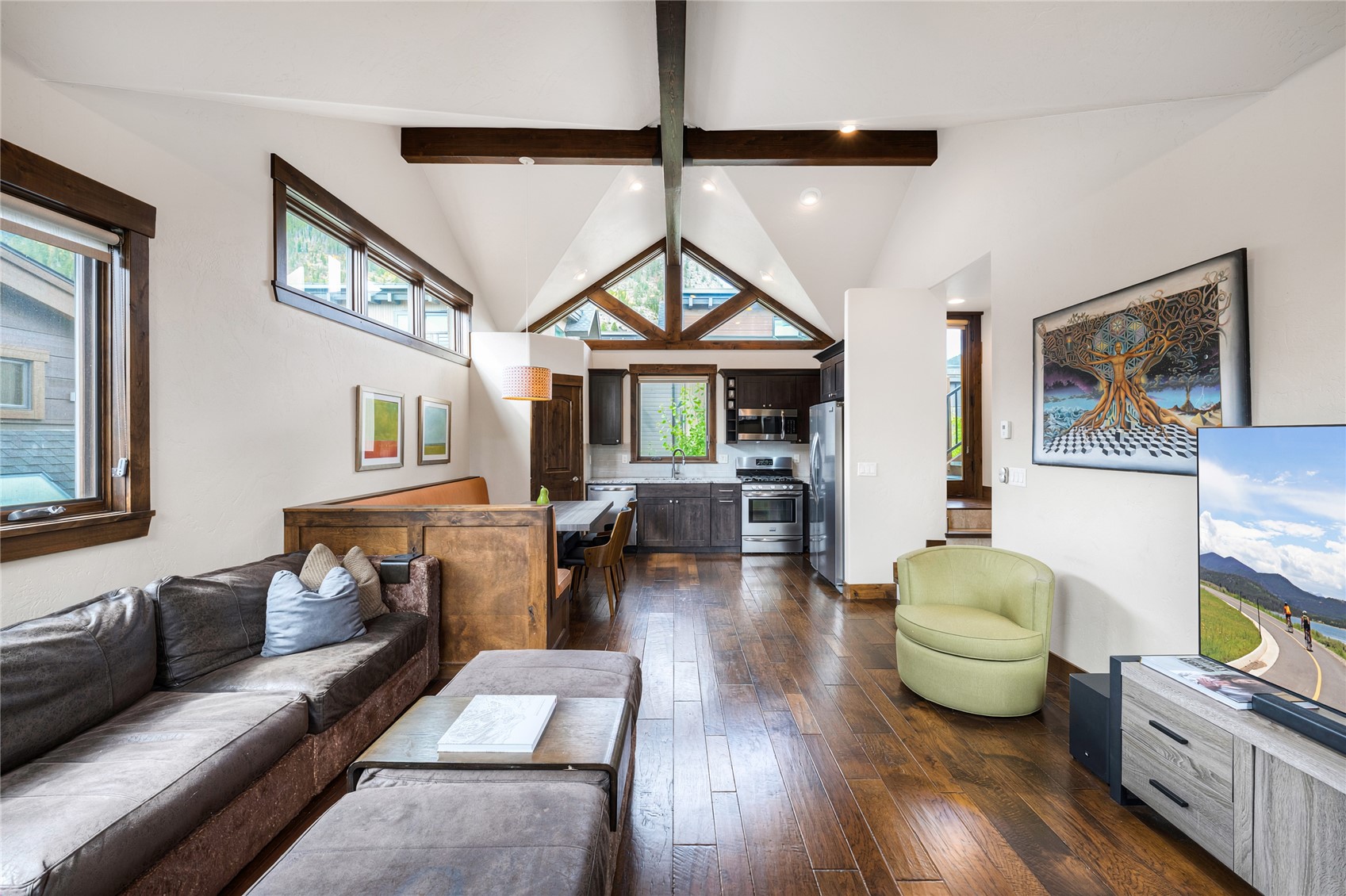Open-plan living room and kitchen with vaulted beam ceiling, triangular windows, and mountain views.