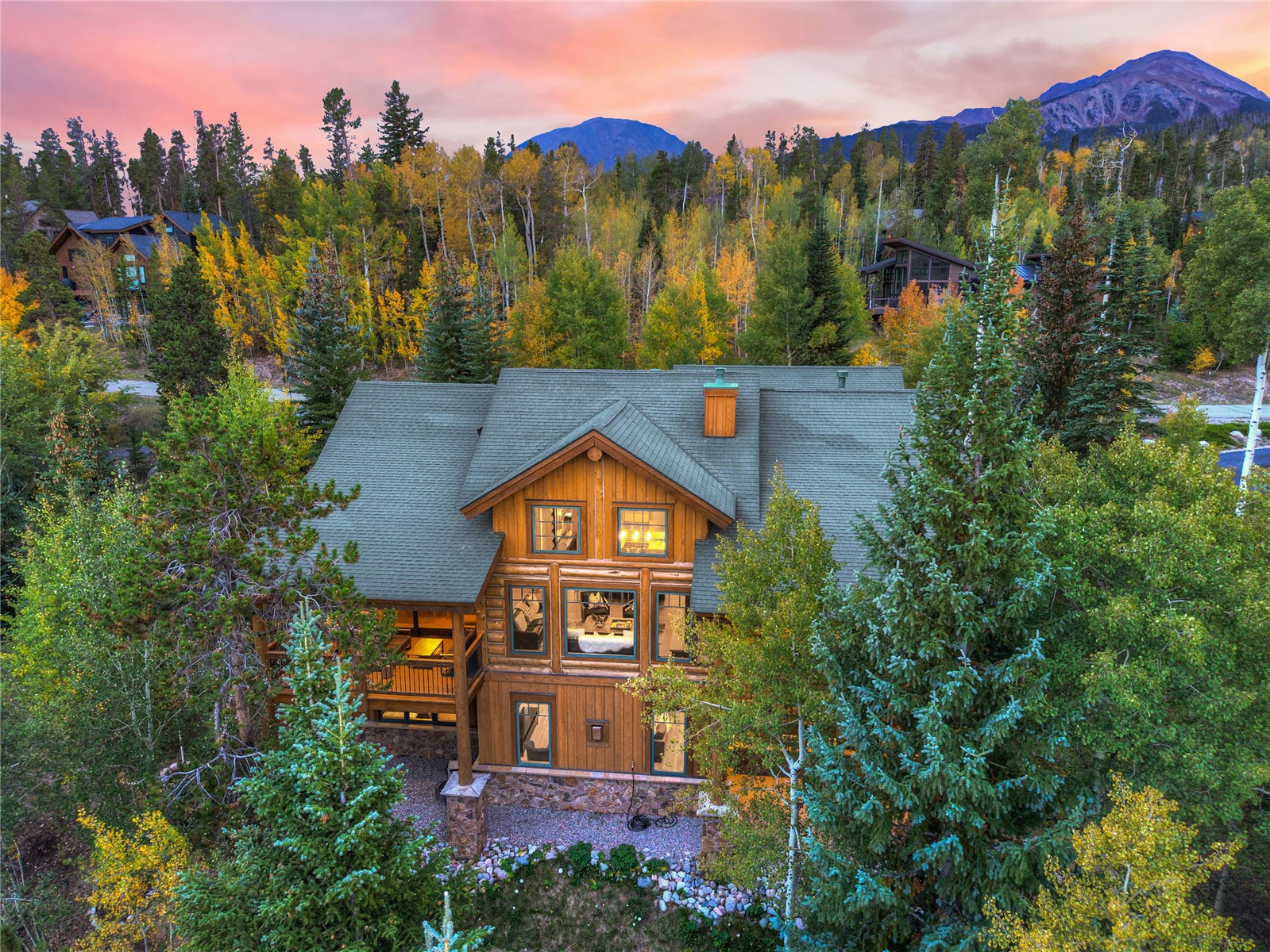 Aerial view of a log home among autumn trees, with mountain peaks in the background.