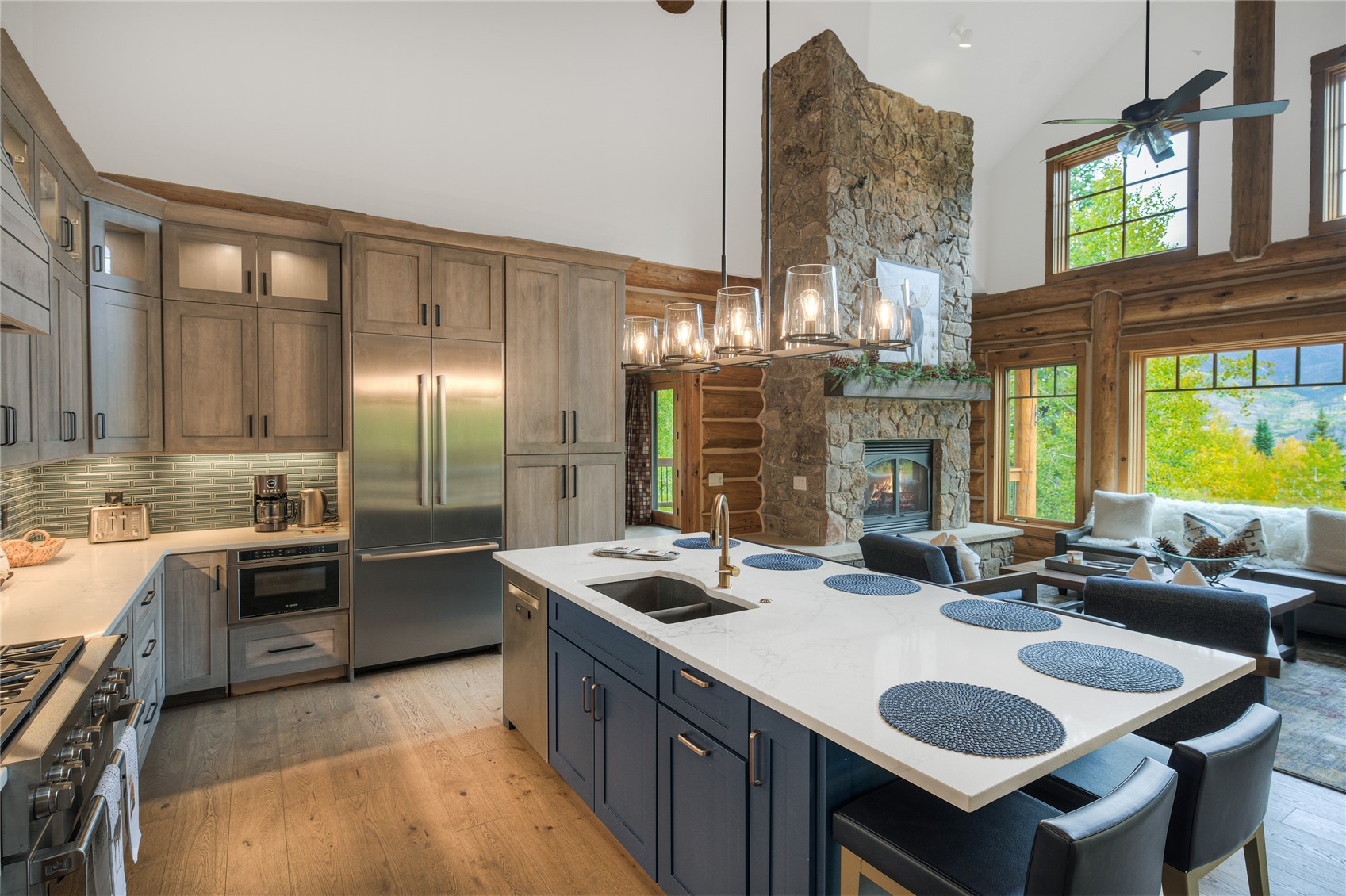Kitchen with a large island, stone fireplace, and mountain views through tall windows.
