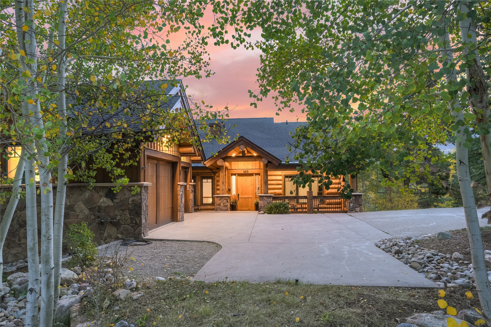 Log home with a stone foundation and covered porch, framed by aspens at dusk.