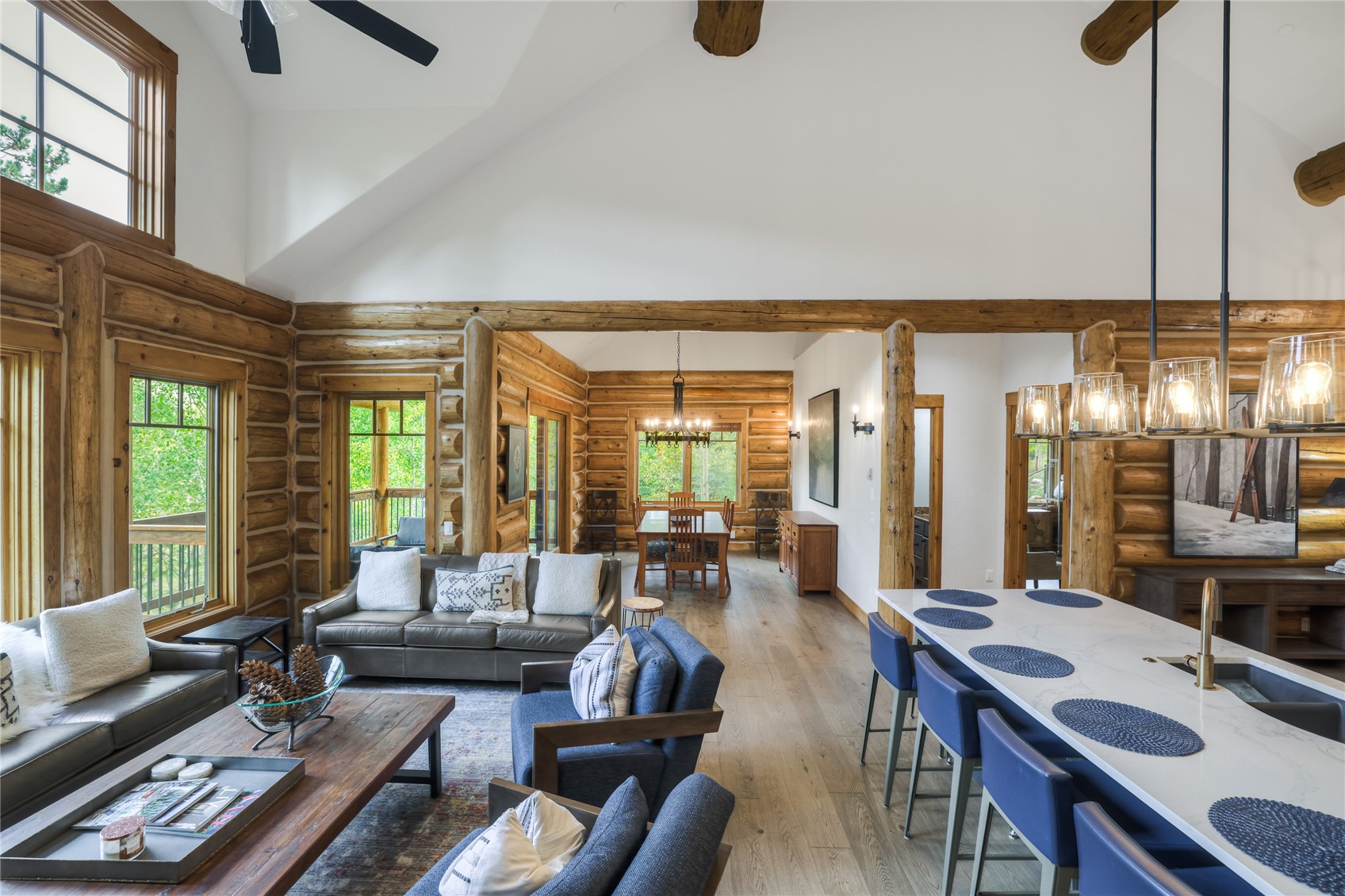 Log home great room with vaulted ceiling, exposed timber beams, and an open living, dining, and kitchen layout.