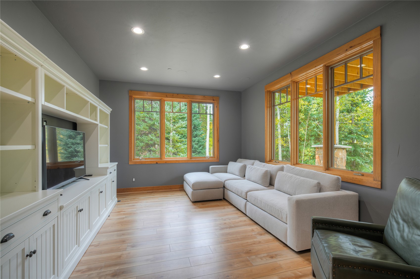 Living room with a white sectional, built-in media cabinetry, and large windows overlooking trees.