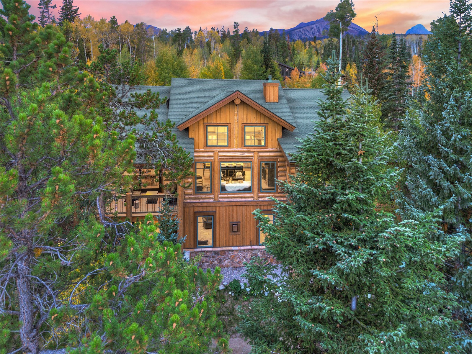 Log cabin nestled among evergreens, with a deck, autumn foliage, and mountain views.