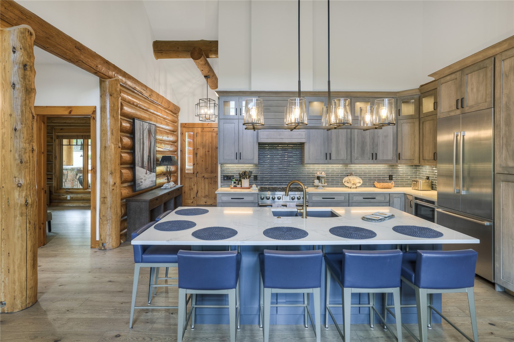 Kitchen with a large white island, blue barstools, gray cabinetry, and rustic log walls.