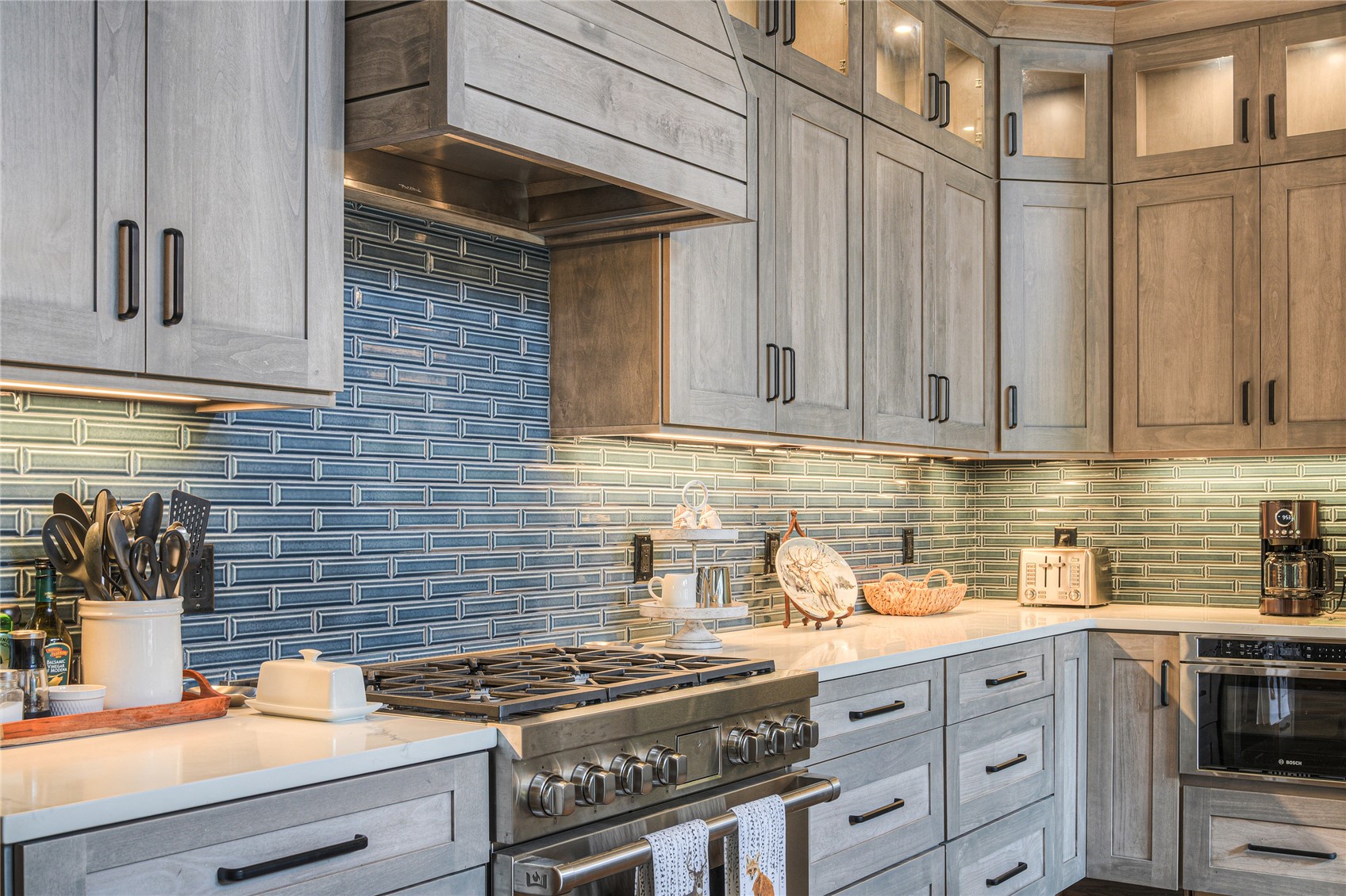 Kitchen with gray wood cabinets, blue tile backsplash, and a large stainless steel range.