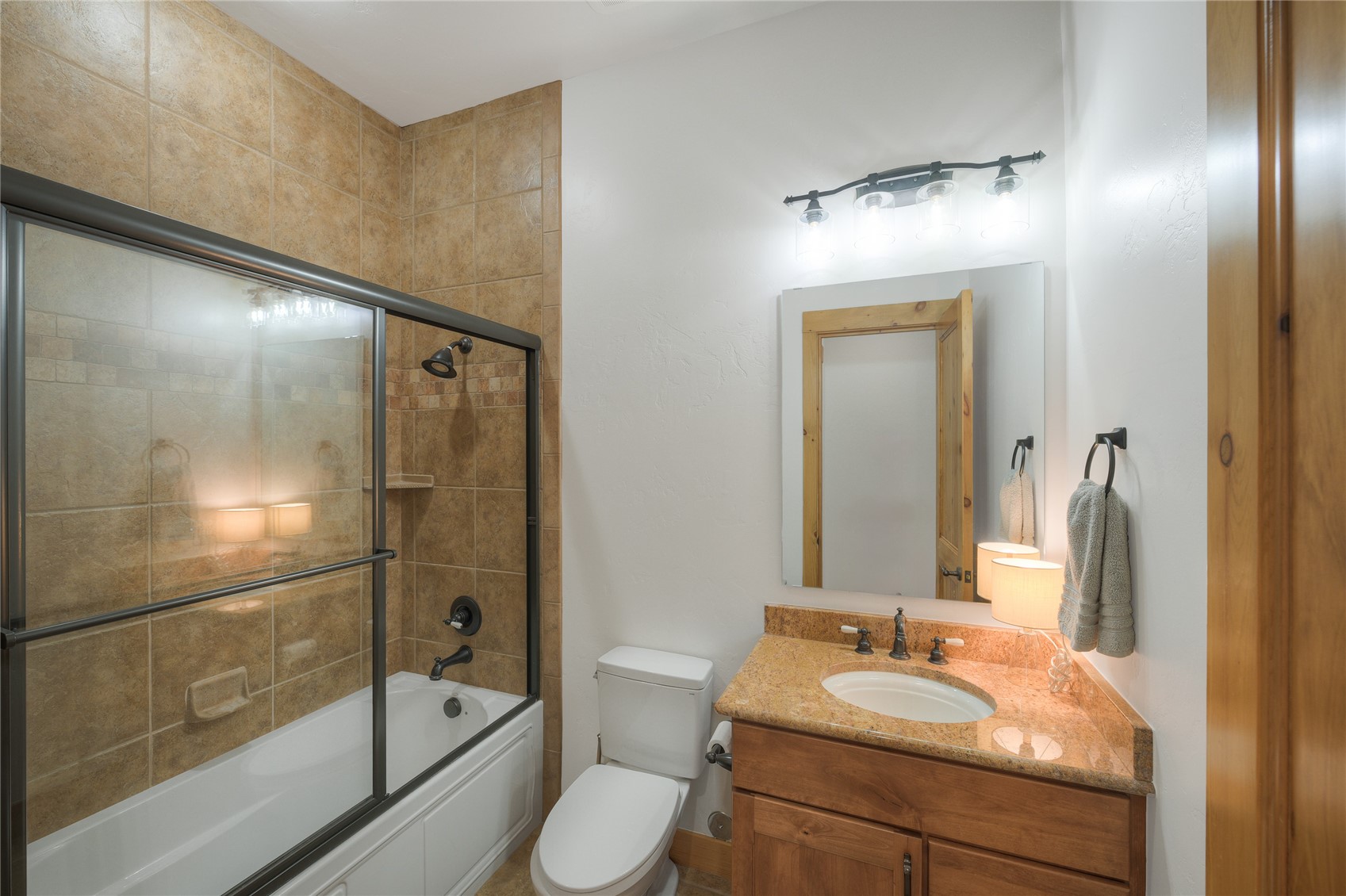 Bathroom with a glass-enclosed tub and shower, tan tile, and a wood vanity with stone countertop.