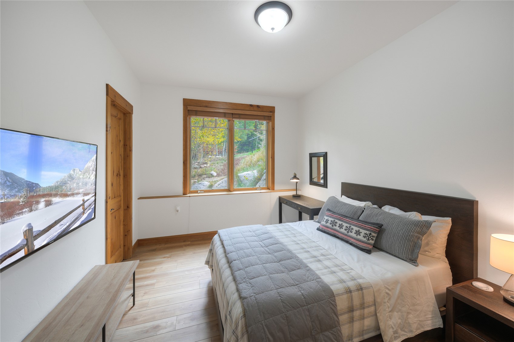 Bedroom with a gray-quilted bed, wood-trimmed window, and hillside view.