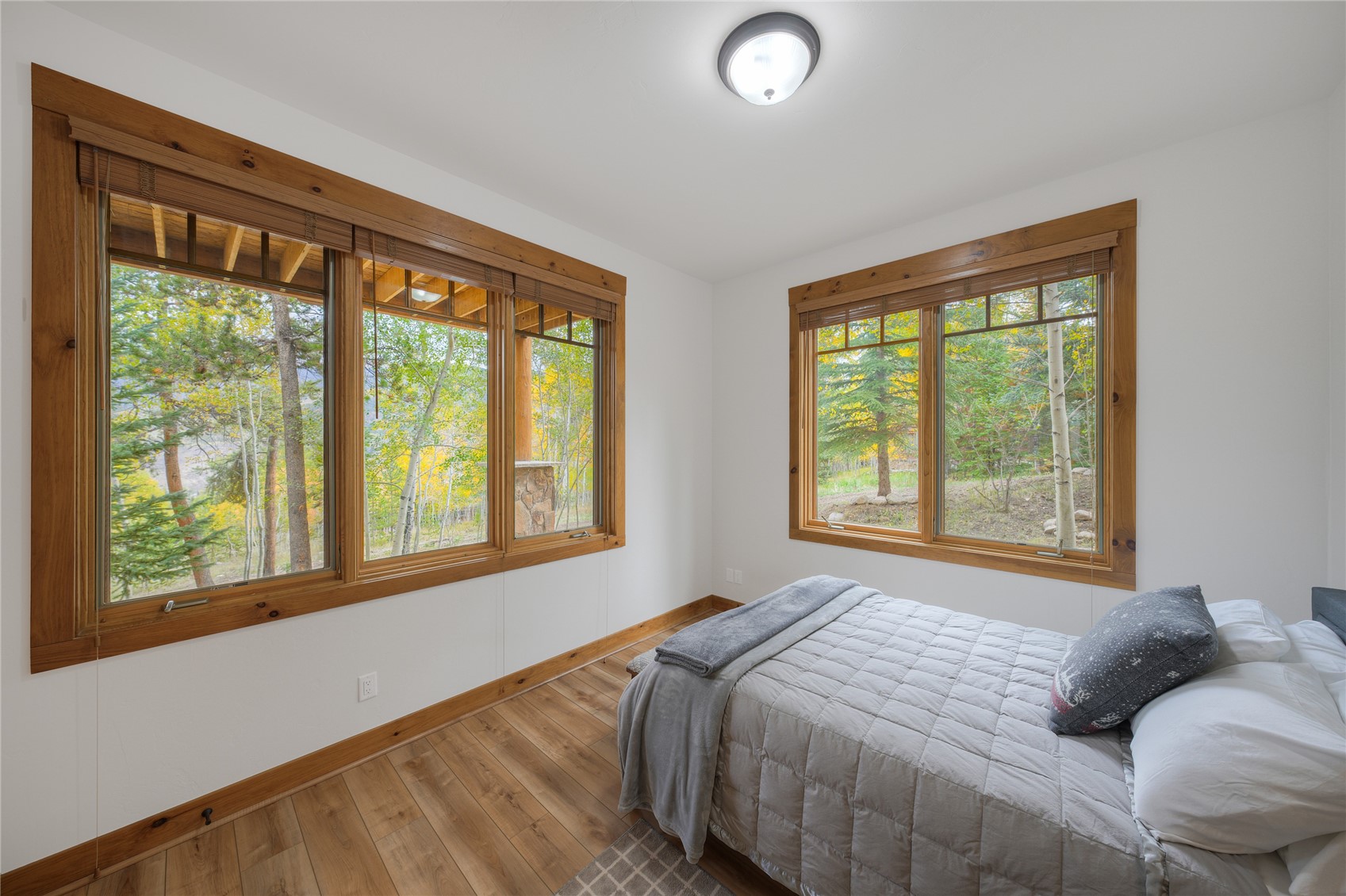 Bedroom with a white quilted bed and large windows overlooking autumn trees.