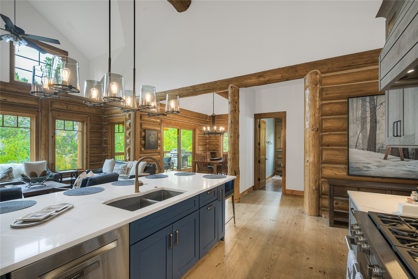 Log-cabin kitchen with a navy island, exposed timber beams, and windows overlooking leafy trees.
