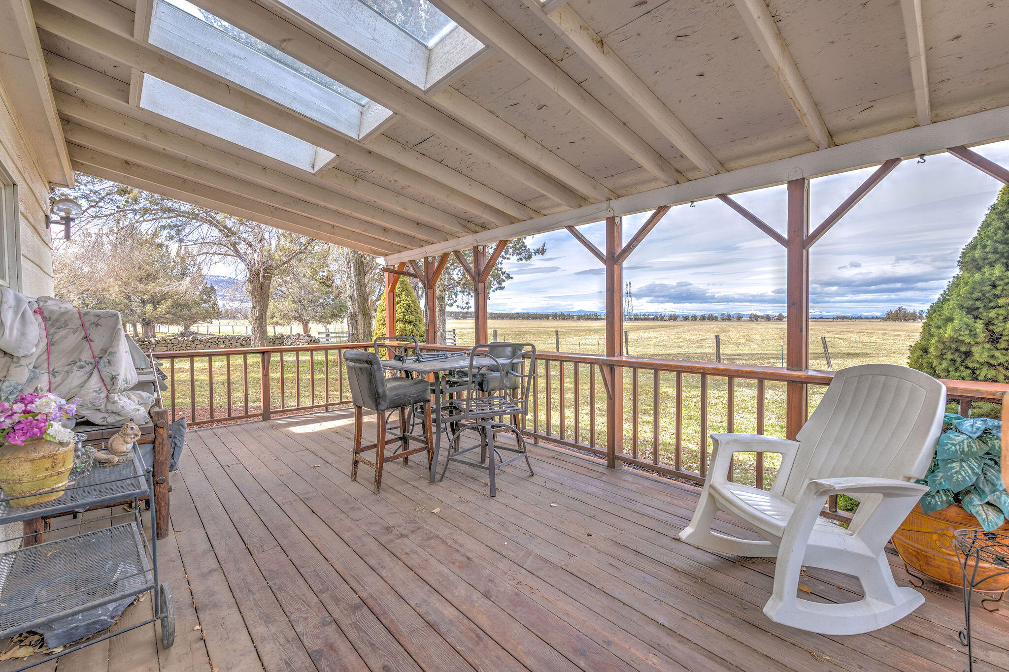 Covered wooden porch with skylights, outdoor seating, and a view across open fields.