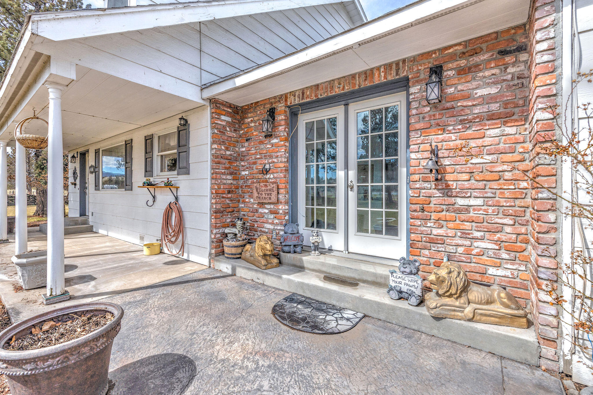 Ranch-house porch with white French doors, red brick walls, and animal statues beside the entrance.