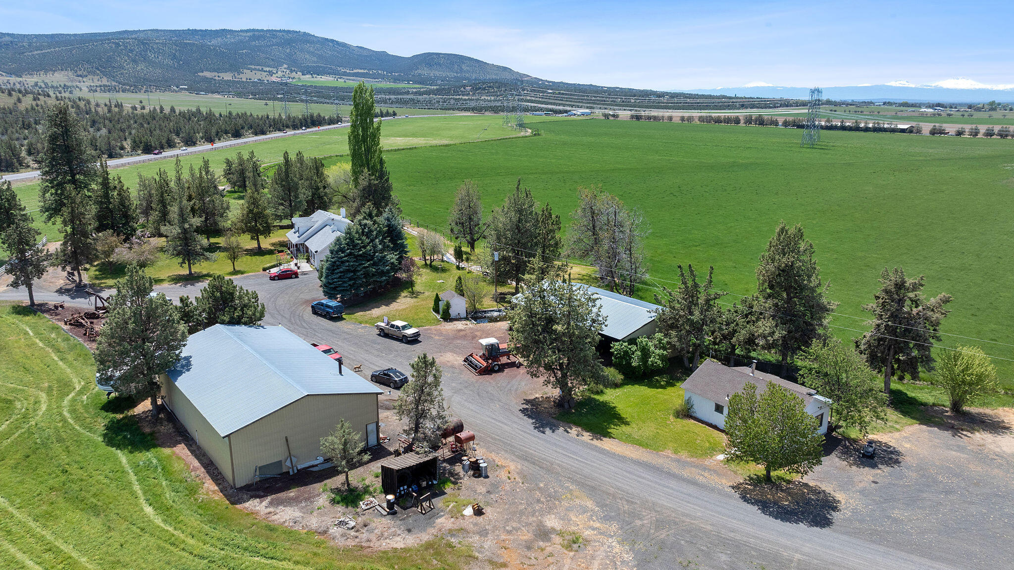 Aerial view of a ranch with a broad green pasture, farm buildings, and distant snow-capped mountains.