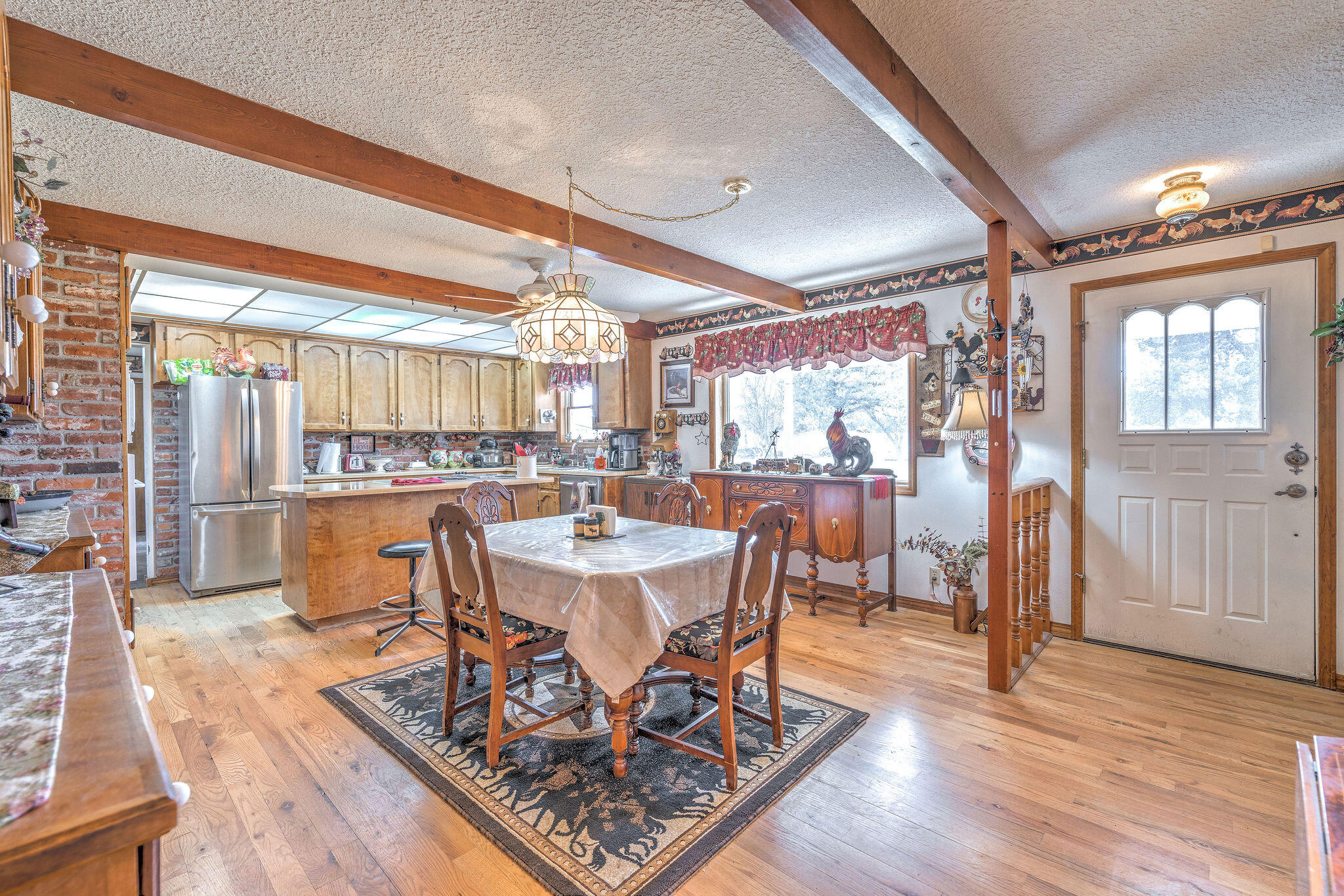 Kitchen and dining area with exposed beams, brick accents, wood cabinetry, and a central dining table.