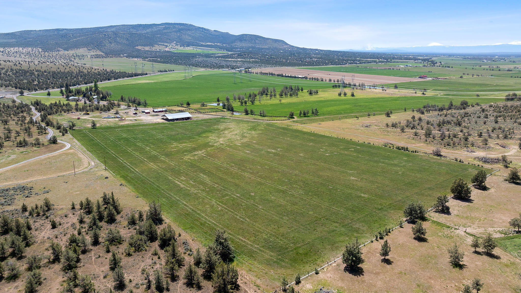 Ranch acreage with expansive green fields, farm buildings, and mountain views.