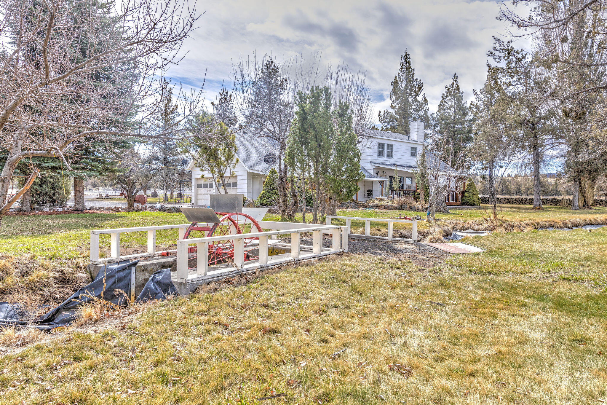 White two-story house behind a grassy yard, with a red water wheel beside a small water channel.