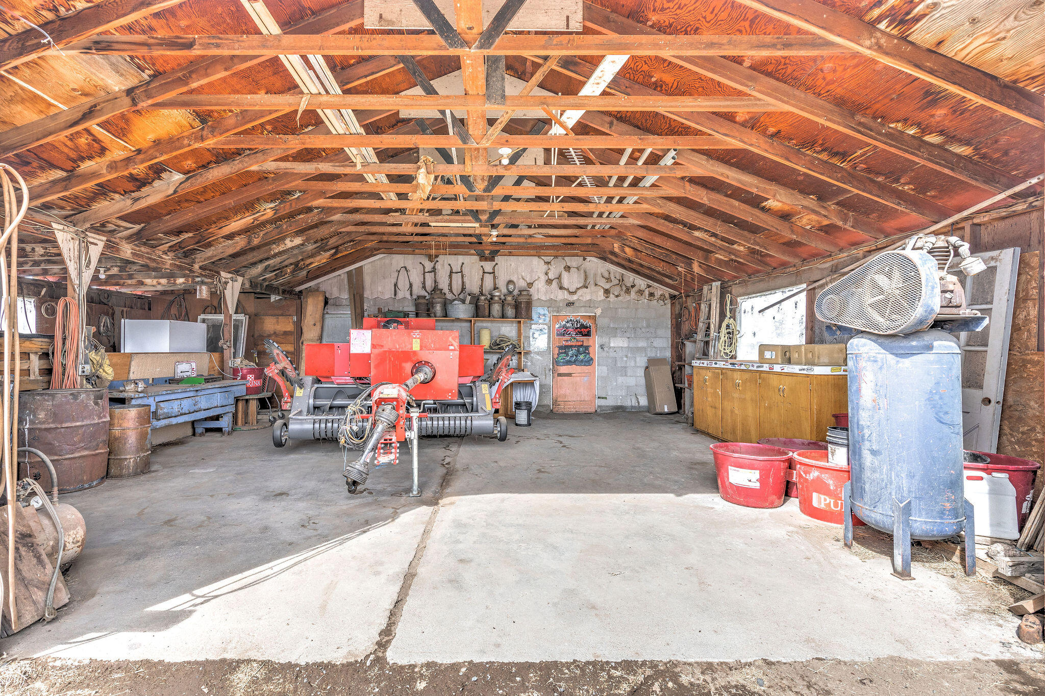 Barn workshop with exposed timber trusses, red agricultural machinery, and a large blue air compressor.