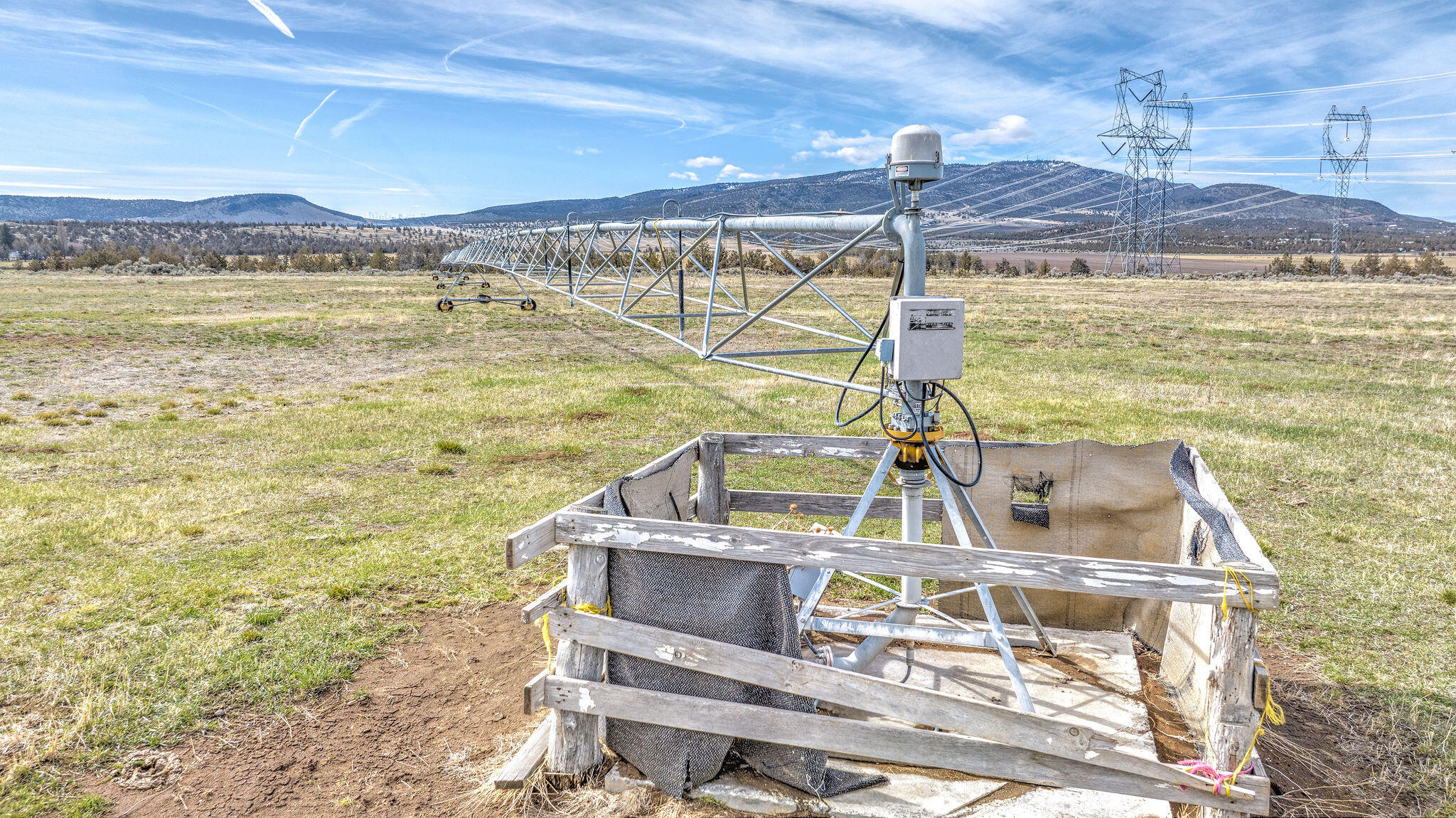 Center-pivot irrigation equipment in an open field, with mountain ridges and power lines beyond.