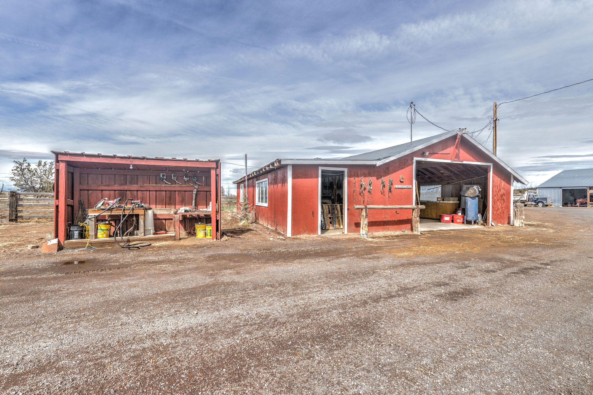 Red ranch workshop with an open equipment bay and covered outdoor work area.
