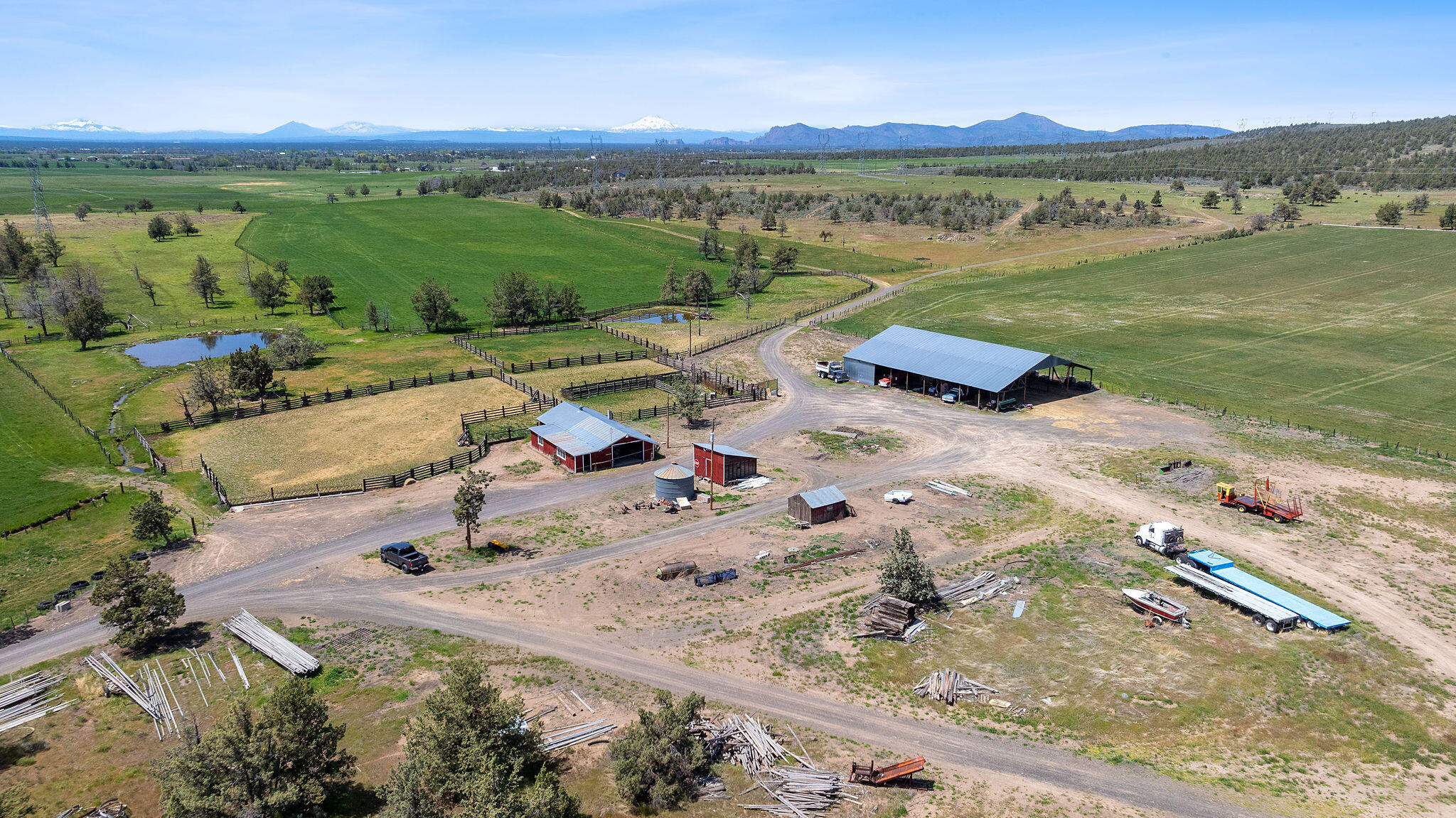 Aerial panorama of a ranch with fenced pastures, ponds, barns, and mountains on the horizon.