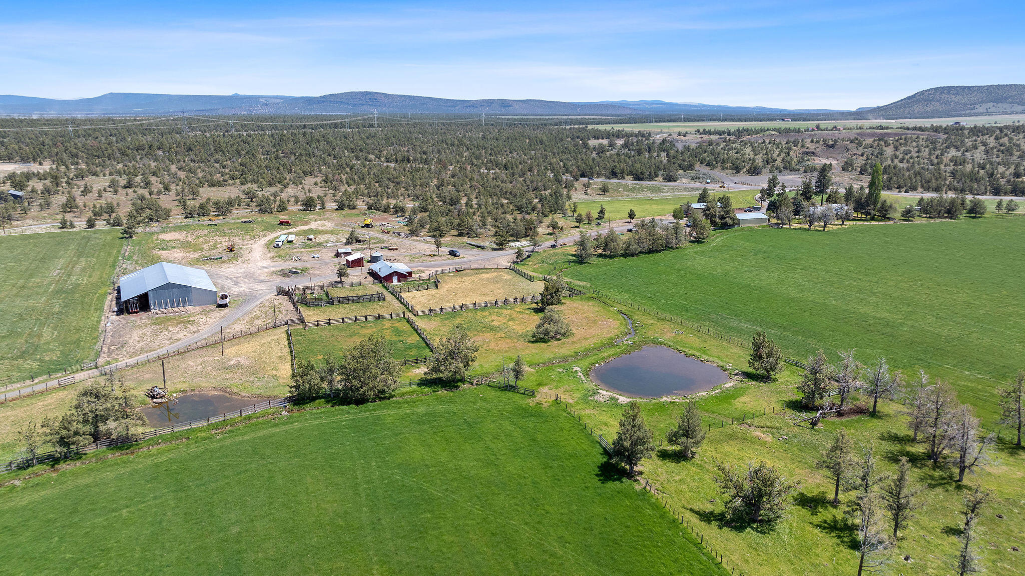Aerial view of a ranch with green pastures, fenced paddocks, barns, and two ponds.
