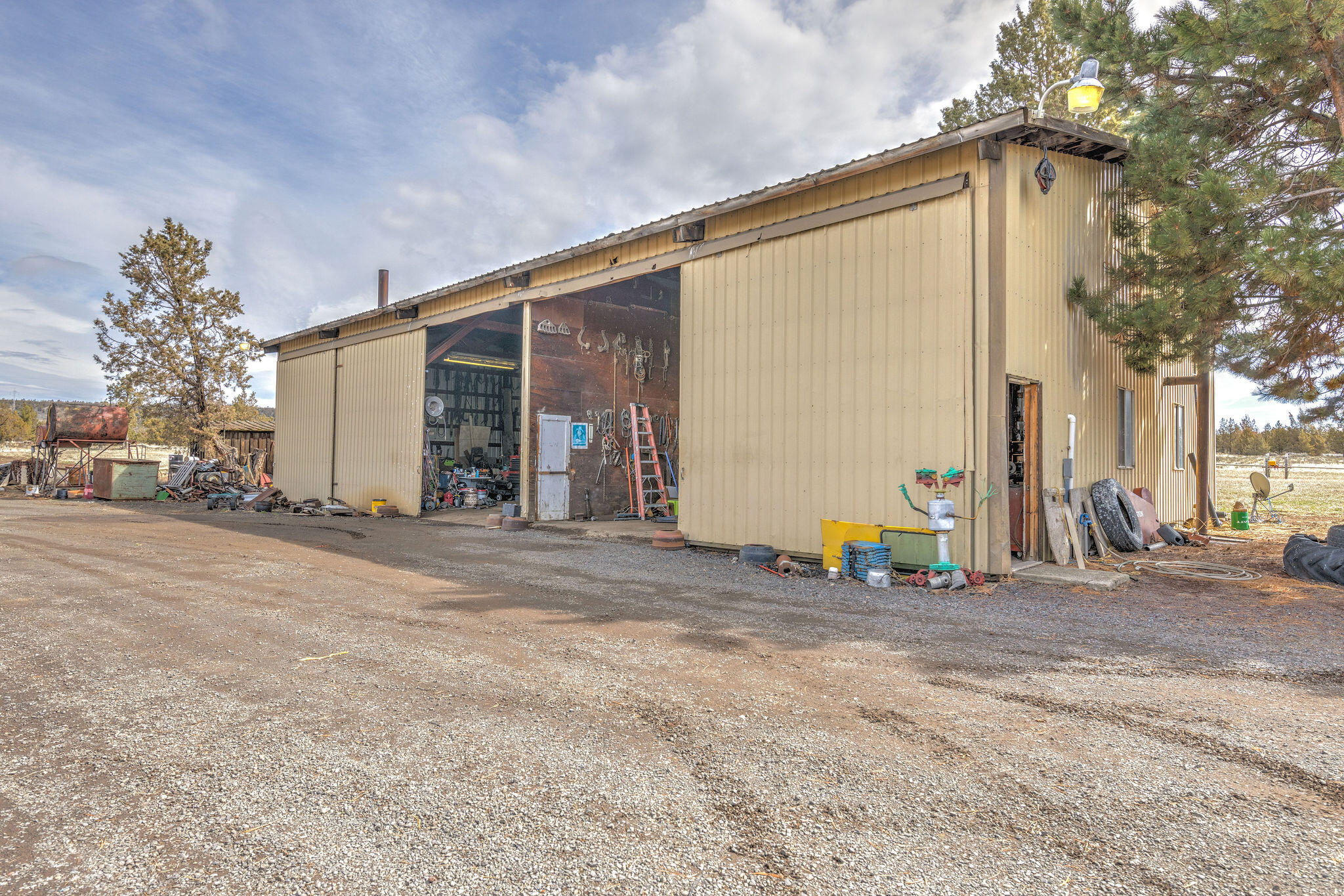 Tan metal workshop with open work bays and equipment scattered around the gravel yard.
