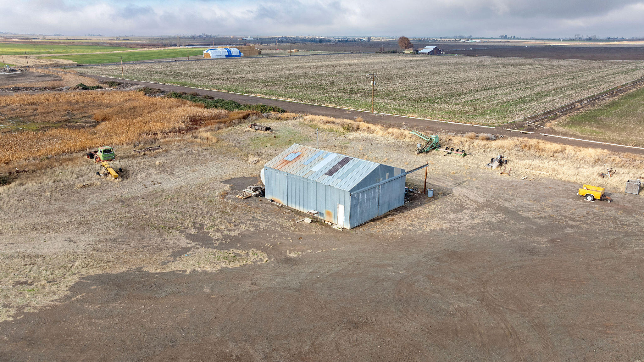 Aerial view of farmland with a metal shed and farm equipment surrounded by broad fields.