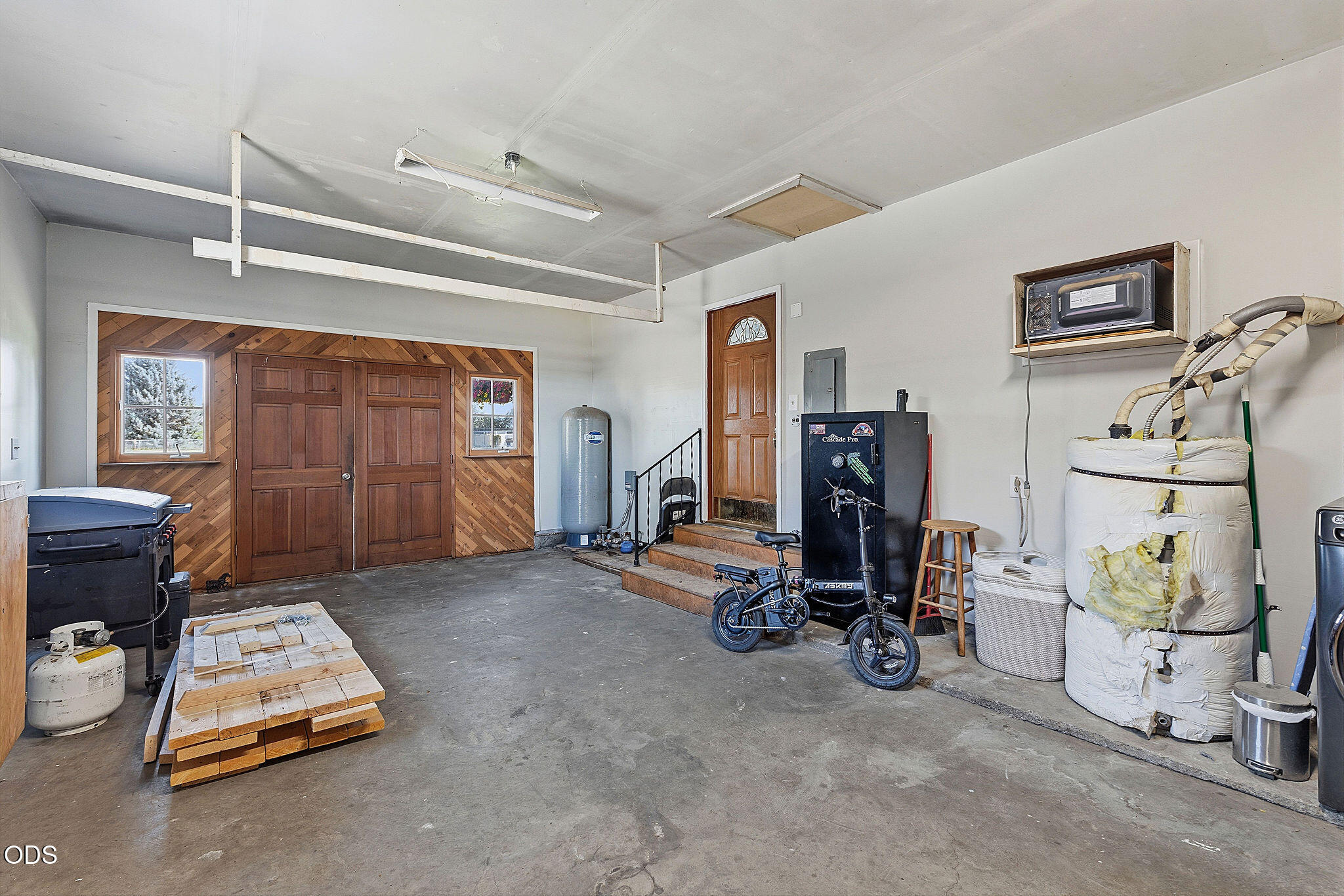 Garage workshop with concrete floor, wood-paneled double doors, and visible utility equipment.